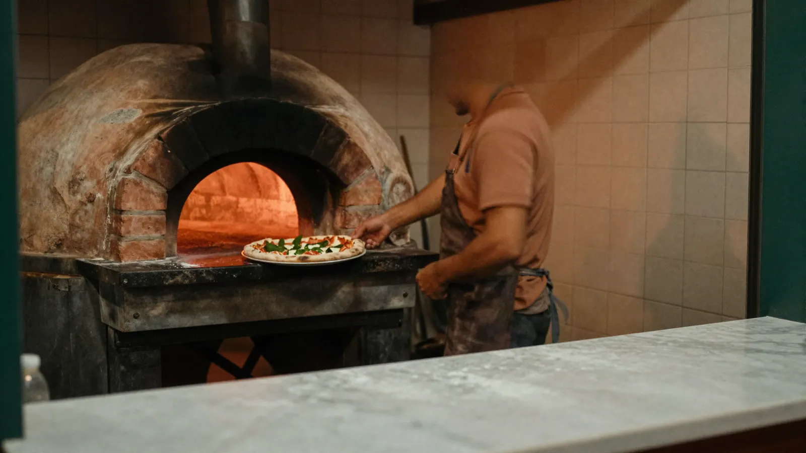 Pizzaiolo colocando uma pizza no forno a lenha.