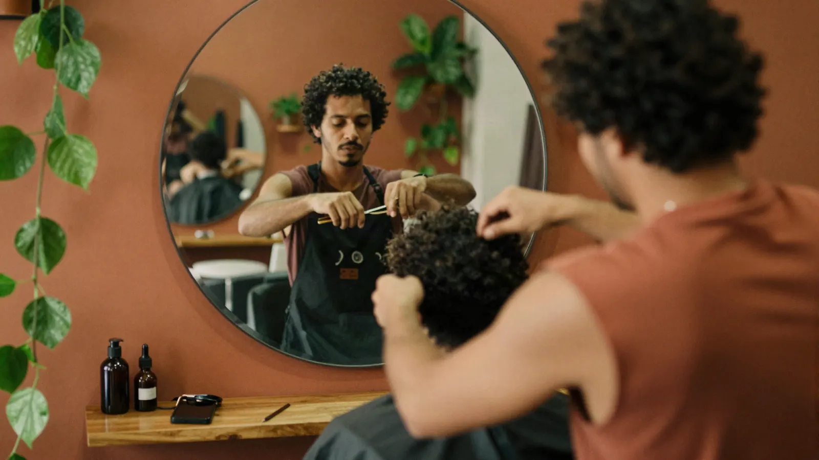 Cabeleireiro cortando o cabelo cacheado de um cliente.